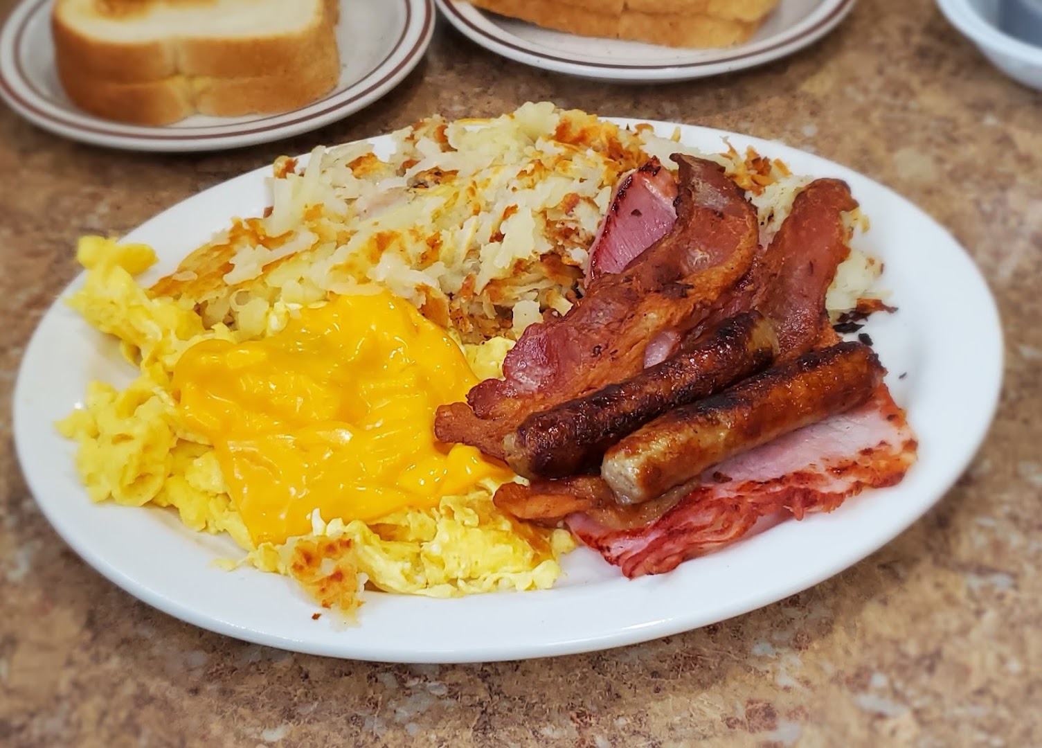 A Liz's breakfast plate with scrambled eggs and cheese, bacon, sausage links and fresh-shredded hash browns