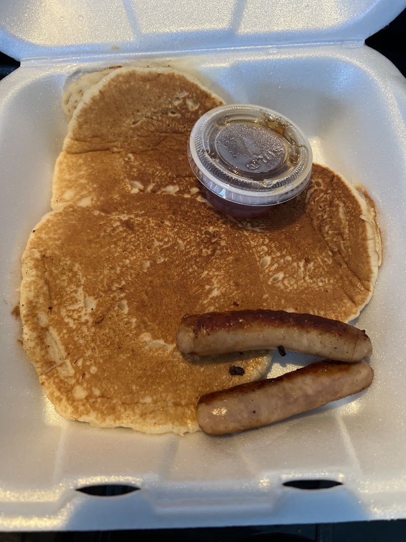 A stack of pancakes with sausage links and a side of syrup
